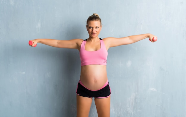 Blonde pregnant woman doing sport making weightlifting