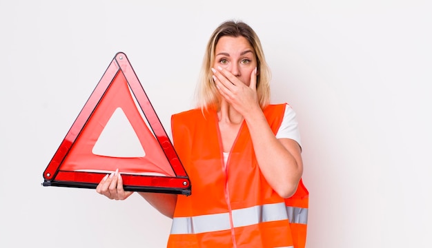 ショックを受けた車の三角形の事故の概念で手で口を覆う金髪のきれいな女性