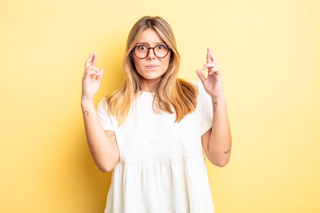 Blonde pretty woman crossing fingers anxiously and hoping for good luck with a worried look