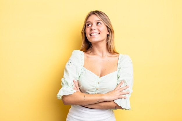 Blonde pretty woman feeling happy, proud and hopeful, wondering or thinking, looking up to copy space with crossed arms