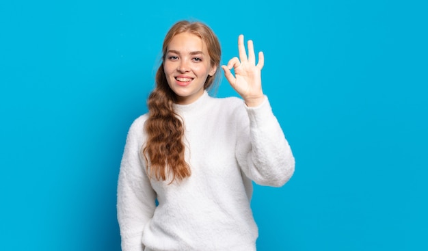 Blonde pretty woman feeling happy, relaxed and satisfied, showing approval with okay gesture, smiling