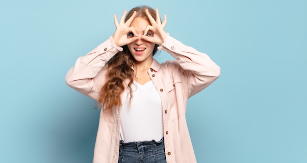 Blonde pretty woman feeling shocked, amazed and surprised, holding glasses with astonished, disbelieving look