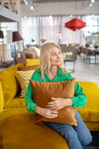 Blonde pretty woman in a green blouse sitting with a pillow