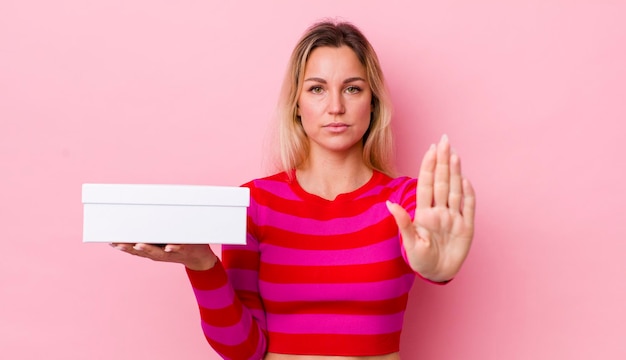 Blonde pretty woman looking serious showing open palm making stop gesture white box concept