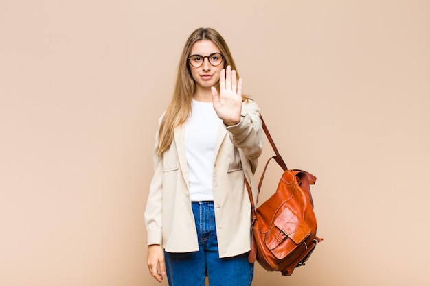 Blonde pretty woman looking serious, stern, displeased and angry showing open palm making stop gesture