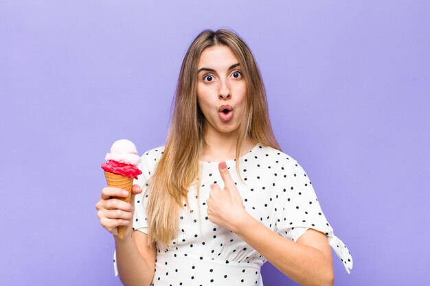 Blonde pretty woman looking shocked and surprised with mouth wide open, pointing to self