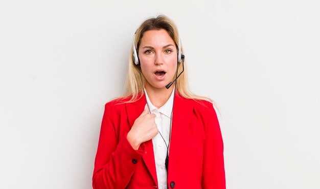 Blonde pretty woman looking shocked and surprised with mouth wide open pointing to self