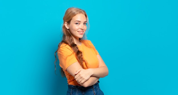 Blonde pretty woman smiling to camera with crossed arms and a happy, confident, satisfied expression, lateral view