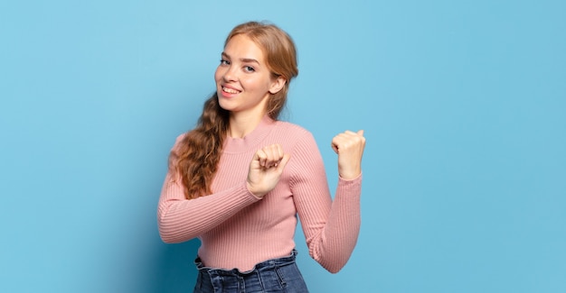 Blonde pretty woman smiling cheerfully and casually pointing to copy space on the side, feeling happy and satisfied