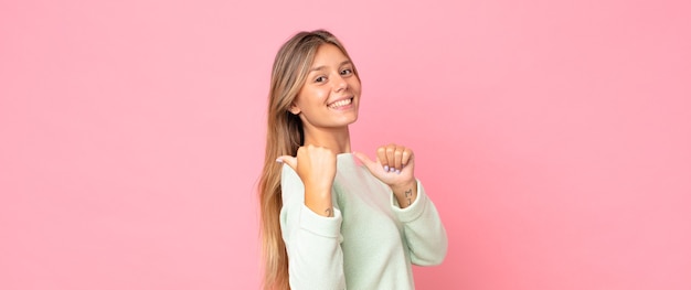 Blonde pretty woman smiling cheerfully and casually pointing to copy space on the side, feeling happy and satisfied