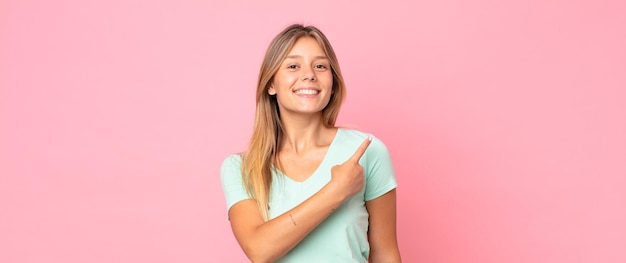 Blonde pretty woman smiling cheerfully, feeling happy and pointing to the side and upwards, showing object in copy space