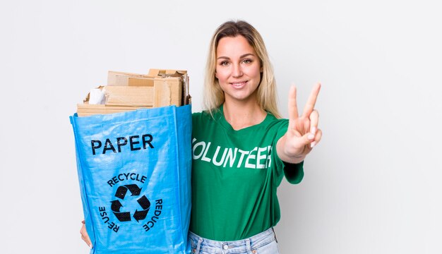 Blonde pretty woman smiling and looking happy gesturing victory or peace recycle concept