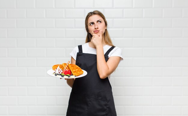 생각하고, 의심스럽고 혼란스럽고, 다른 옵션을 사용하여 어떤 결정을 내릴지 궁금해하는 금발의 예쁜 여자