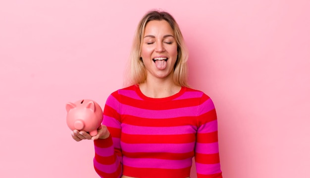 Blonde pretty woman with cheerful and rebellious attitude joking and sticking tongue out piggy bank concept