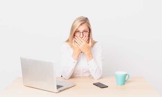 blonde pretty woman young blonde woman covering mouth with hands with a shocked and working with a laptop