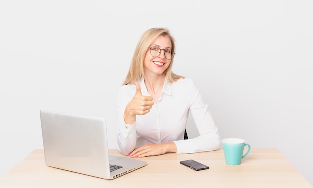 Blonde pretty woman young blonde woman feeling proud,smiling positively with thumbs up and working with a laptop