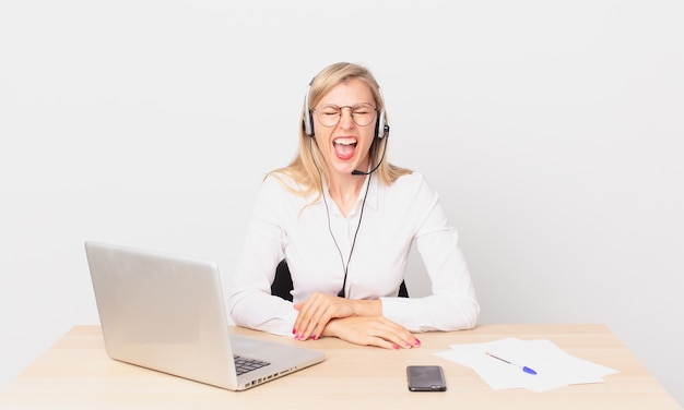 Blonde pretty woman young blonde woman shouting aggressively, looking very angry and working with a laptop