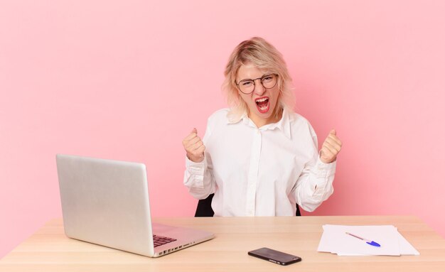 Blonde pretty woman young pretty woman shouting aggressively with an angry expression. workspace desk concept