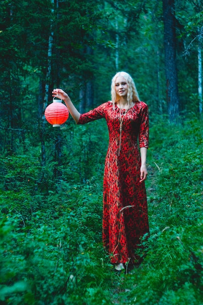 彼女の手に赤いちょうちんを持った森の赤いドレスを着た金髪