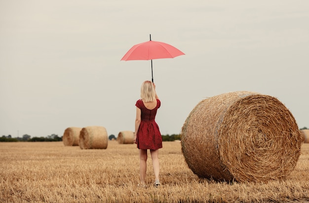 Blonde in a red dress with an umbrella in a wheat field before the rain