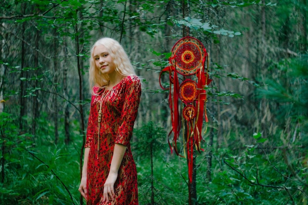 Blonde in a red dress in the woods next to a dreamcatcher