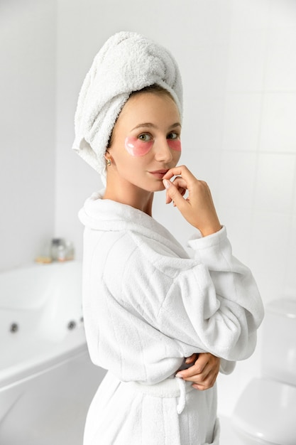 Blonde schattige jonge vrouw met roze ooglapjes in witte badkamer