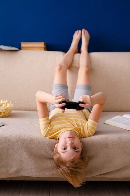 Blonde schoolboy boy plays video games holds a gamepad eats popcorn instead of learning lessons