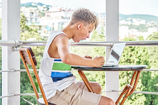 Blonde schooljongen viert overwinning met moeilijk videospelletje op laptop