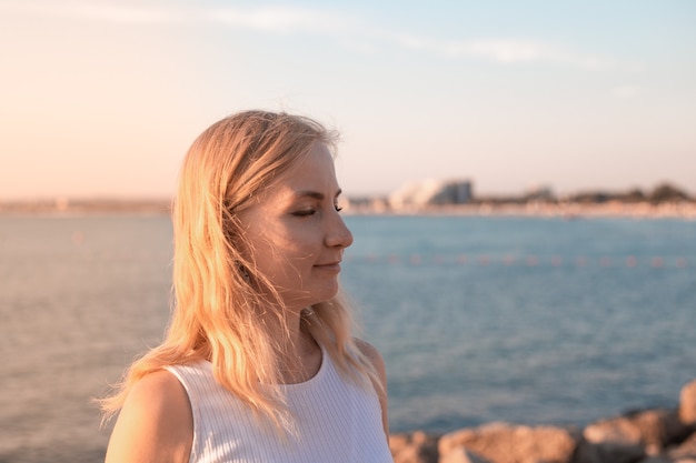 The blonde on the seashore at sunset closed her eyes side portrait closeup summer vacation on the