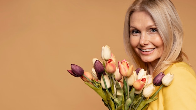 Blonde senior vrouw die lacht en tulpen vasthoudt tegen een gele achtergrond