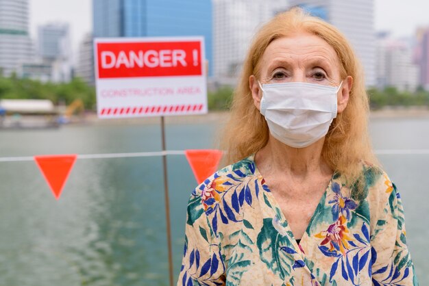 公園で湖のそばの危険の兆候とマスクを身に着けている金髪の年配の女性