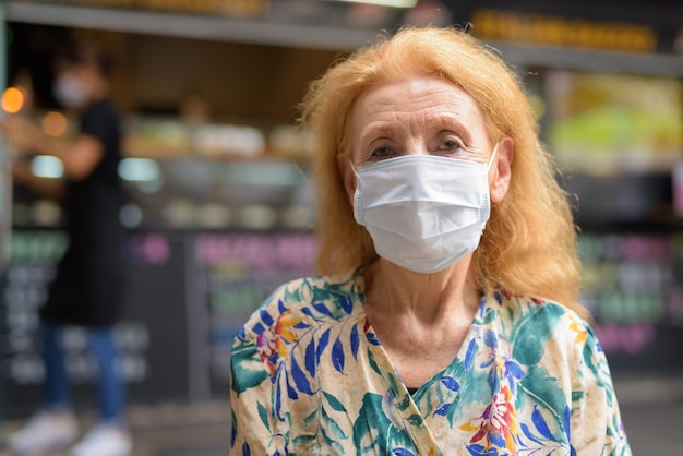 Blonde senior woman with mask for protection from coronavirus outbreak at the coffee shop outdoors