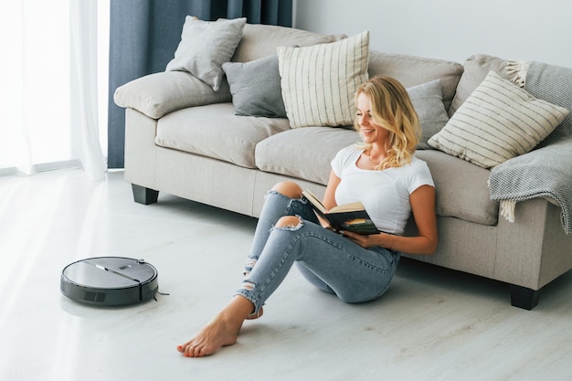 Photo blonde sits on the floor woman in casual clothes is indoors at home