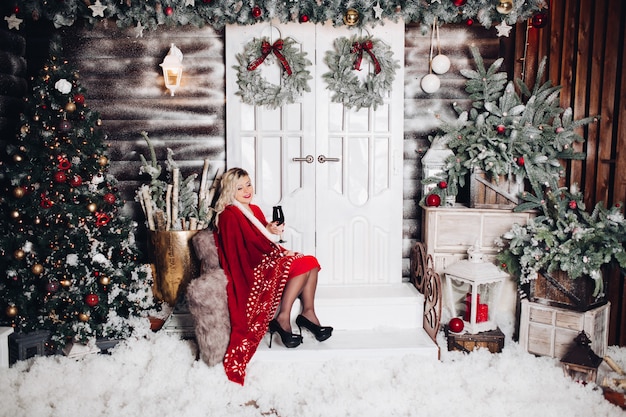 Blonde sitting on stairs decorated for Christmas with glass of vine.