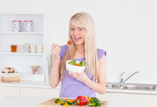 Femmina sorridente bionda che mangia la sua insalata