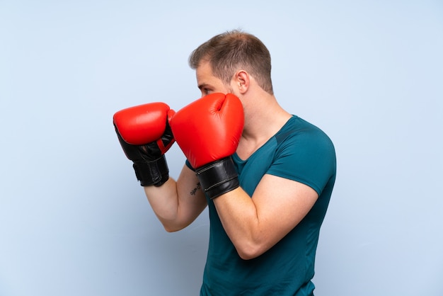 Blonde sport man over blue wall with boxing gloves