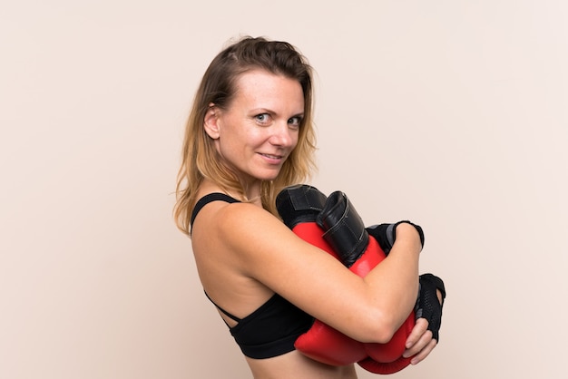 Blonde sport woman over isolated wall with boxing gloves