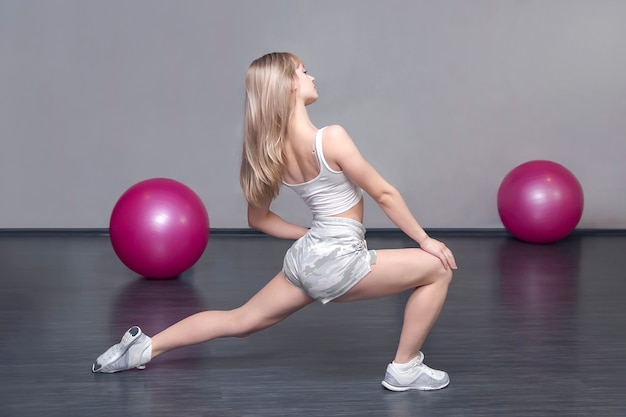 Blonde sportieve blanke dame is in de sportschool tijdens training, oefeningen om de spieren op de benen te strekken. Warming-up voor de training. Fitness voor vrouwen.