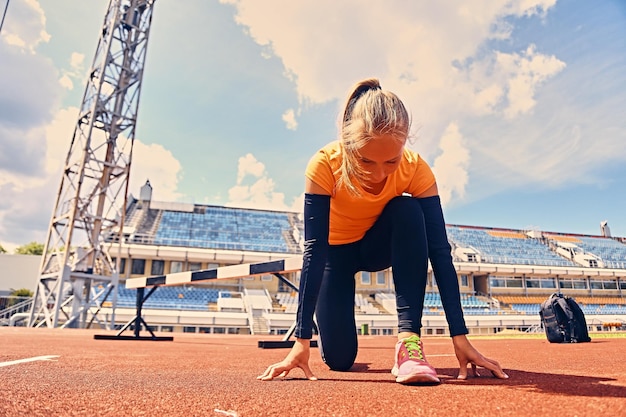 Blonde sportieve vrouwelijke loper naar snelle startpositie op een stadion.