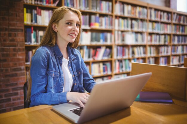 Blonde student die laptop in bibliotheek met behulp van