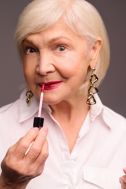 Blonde stylish senior woman putting lip gloss on her lips