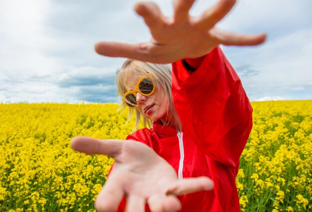 Blonde in sunglasses and red tracksuit in rapeseed field