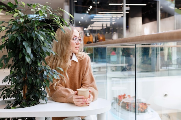 Blonde in a sweater in a shopping mall with coffee