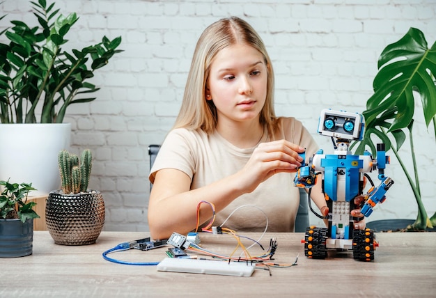 Photo a blonde teen girl building and programming robot while studying robotics engineering and coding