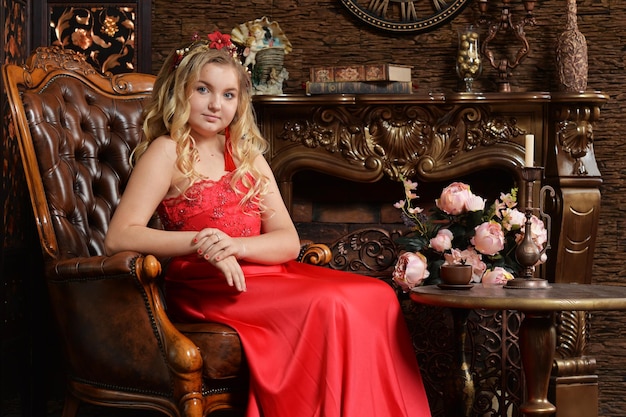 Blonde teenage girl in bright red dress sitting in armchair