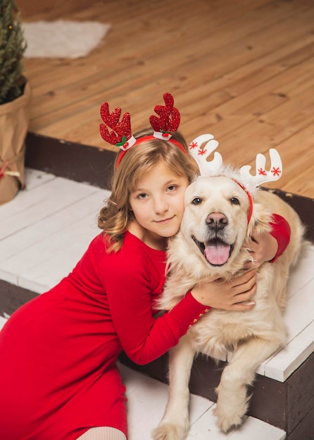 Blonde teenager and her dog with antlers on their heads are hugging on the steps