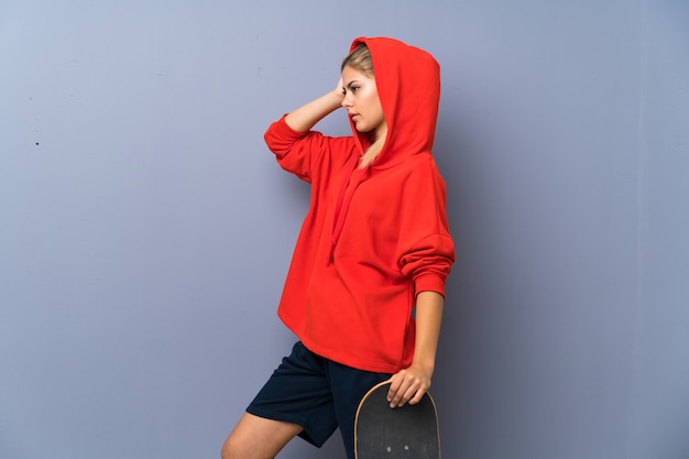 Photo blonde teenager skater girl over grey wall