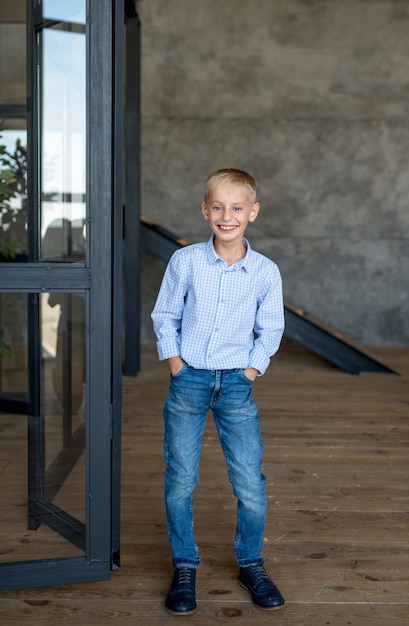 Foto adolescente bionda, in una camicia e jeans alla moda, si trova in un appartamento in stile loft e sorride ampiamente