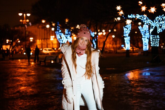 Blonde teenager with long hair in winter clothes on festive winter evening on street closeup portrai...