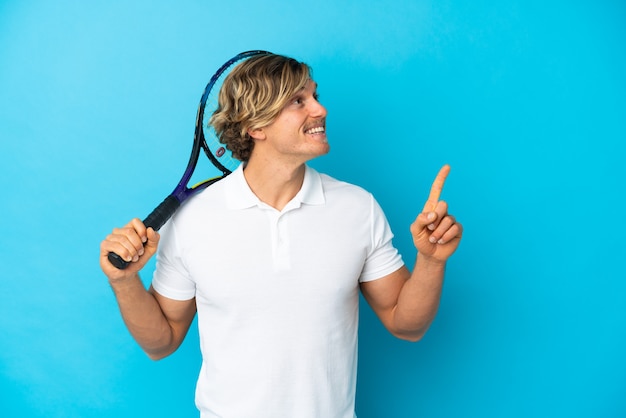 Blonde tennis player man isolated on blue wall pointing up a great idea